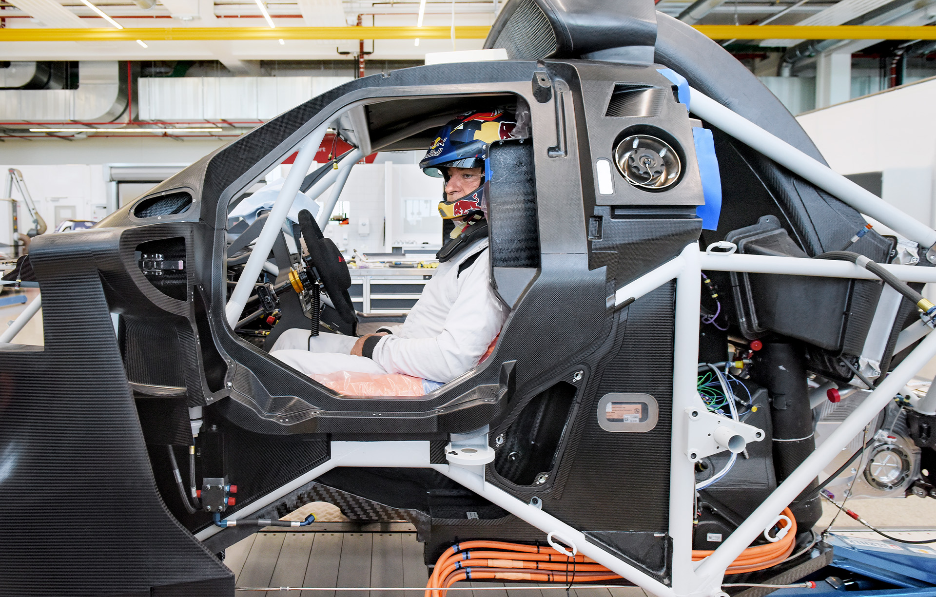 Carlos Sainz, one of Audi Sport’s Dakar Rally drivers, in the cage of the rally car at the seat fitting. He sits behind the wheel on an orange foam cushion. 